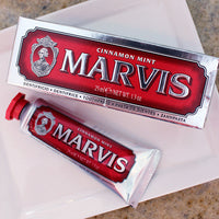 Travel-size tube of Marvis toothpaste with the lid off, displayed on a white plate with a decorative background.