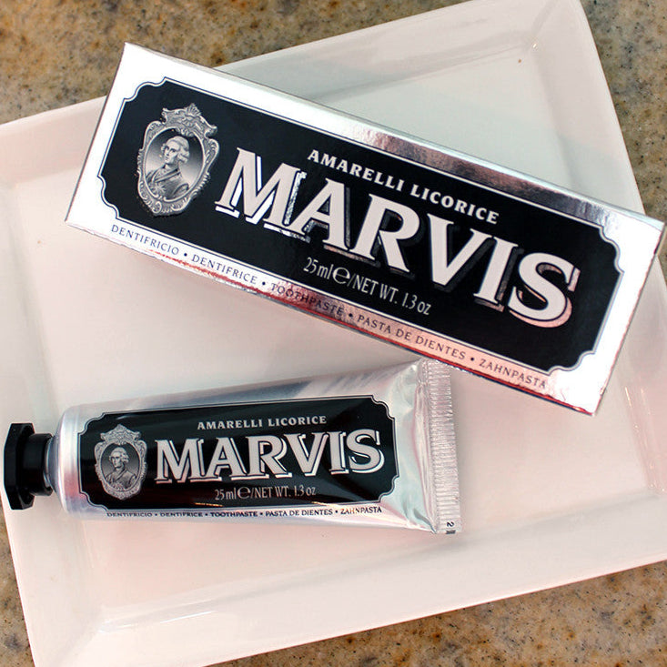 Travel-size tube of Marvis toothpaste with packaging, displayed on a white plate with a blurred background.