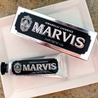 Travel-size tube of Marvis toothpaste with packaging, displayed on a white plate with a blurred background.