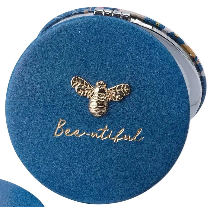 Three views of a round compact mirror with a blue velvet cover and a bee-themed printed interior. One view shows the closed cover with a gold bee emblem and the word 'Beautiful' in gold script.