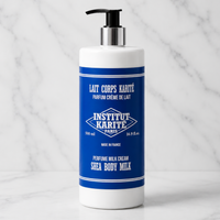 A 500 ml white pump bottle of Institut Karite Paris Shea Body Milk with a blue label, set against a white marble background.
